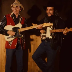 THEY CALLED HIM A REBEL. WAYLON CALLED HIM A GENIUS. They called him too wild for radio. Too loud, too unpredictable, too funny to fit the rules of Nashville. But to Waylon Jennings, Jerry Reed wasn’t a rebel — he was a reminder that music was supposed to be alive. One night after a late studio jam, Waylon laughed so hard he almost dropped his cigarette. “You’re the happiest outlaw I’ve ever met, Jerry,” he said, grinning. “You argue with judges, break every rule in town — and people still clap for you.” Reed just shrugged that mischievous smile of his. “Guess that’s because I don’t sing for the law, brother. I sing for the folks who break it with a smile.” When “When You’re Hot, You’re Hot” hit No. 1, Waylon sent him a bottle of Tennessee whiskey with a note: “You’re still guilty, but damn — you’re guilty of making us all proud.” That was Jerry Reed: a man who could turn trouble into laughter, and laughter into legend. Even in a town full of outlaws, he was the only one who got away with it — smiling. Featured image
