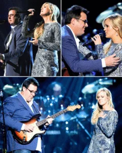 “40,000 PEOPLE… AND ONE MOMENT THAT MADE AN ENTIRE ARENA FORGET TO BREATHE.” No one in that arena knew what was coming. One second, it was quiet enough to hear someone take a slow breath. Then Carrie Underwood stepped into the light, her voice soft at first, almost like she was singing to herself. But it kept rising — warmer, stronger — the kind of sound that makes you look up without even knowing why. And then Vince Gill joined her. His guitar wasn’t loud or flashy. It was gentle, steady, the kind of tone that wraps around a moment and holds it still. Together, they turned “How Great Thou Art” into something that didn’t feel like a song anymore — it felt like a prayer. When Carrie reached that final note, people didn’t cheer right away. They just stood there, hands shaking, eyes wet, letting it wash over them. Then the room exploded. Because everyone felt it: Something holy had just happened. Featured image