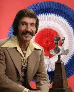 HE SPENT 30 YEARS SINGING ABOUT LEGENDS… THEN LEFT THE WORLD QUIETLY AT 57. Far from the stages where his voice once painted deserts, gunfighters, and broken men, Marty Robbins spent his final birthday in silence. No spotlight. No applause. Just a quiet table, a small cake, and the people who knew him before the songs made him immortal. He looked thinner. Weaker than the cowboy heroes he once sang about. But when someone raised a glass, Marty answered with a gentle smile. No words. No speech. Just a slow nod — the kind that comes from a man who’s already said everything he needed to say in song. For decades, he gave us stories of men who never flinched. Yet in that room, there was no legend left to perform. That night wasn’t a show. It was a quiet farewell… from a man who finally stepped out of the myth he created. 🤍 Featured image